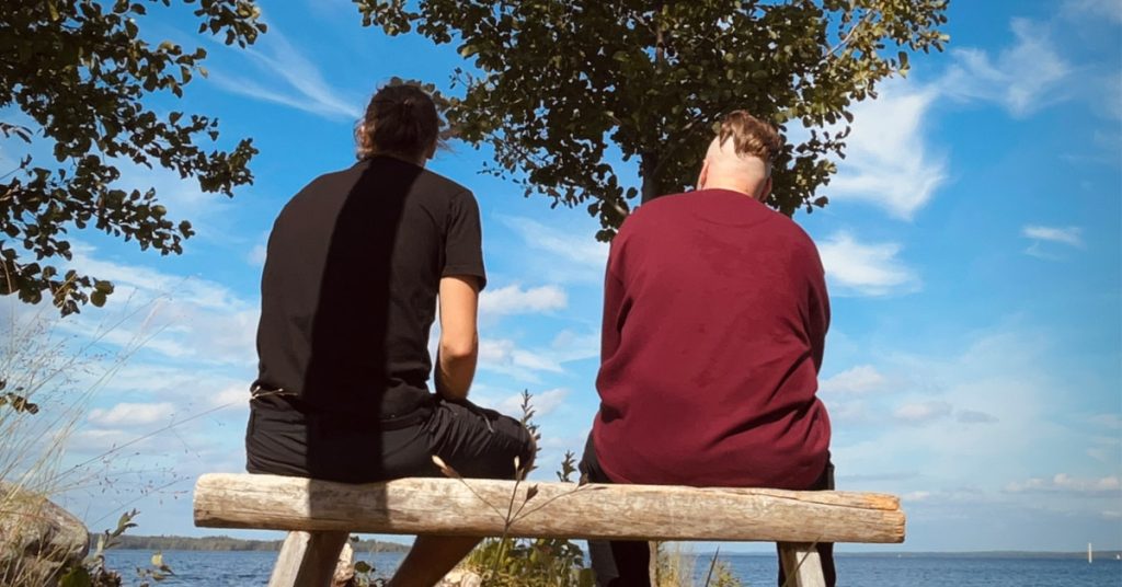 Liikuntaetsivä ja nuori istumassa rannalla.