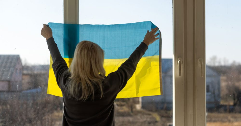 Nainen asettaa Ukrainan lippua ikkunaan.