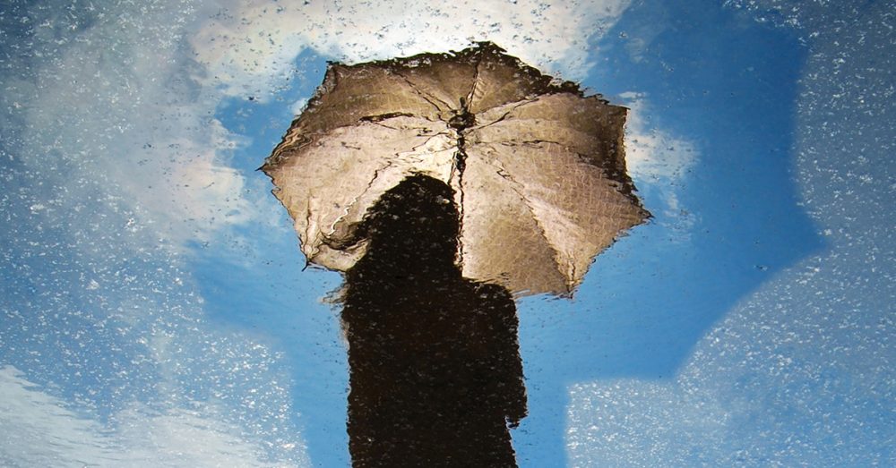 Nuoren ja sateenvarjon kuva heijastuu lätäköstä.