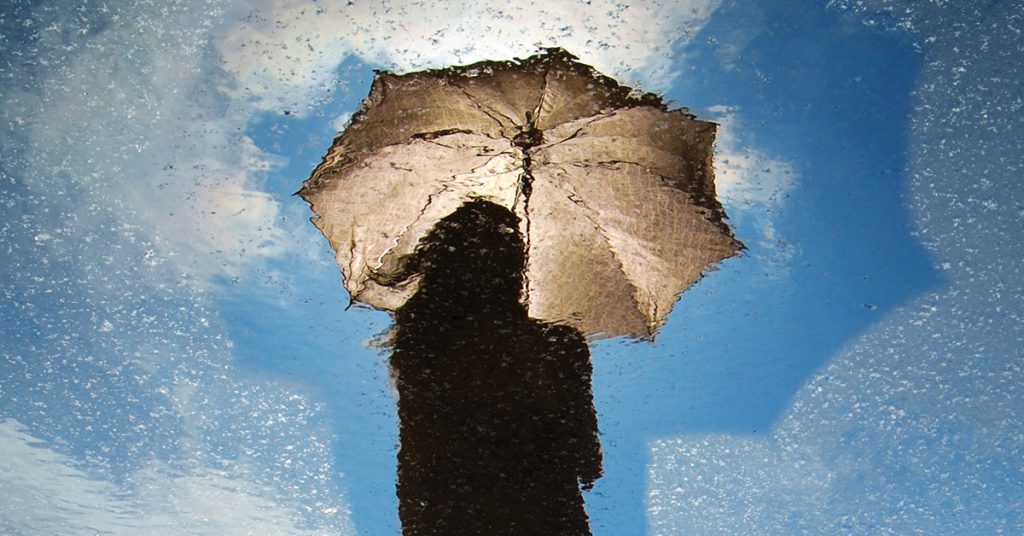 Nuoren ja sateenvarjon kuva heijastuu lätäköstä.