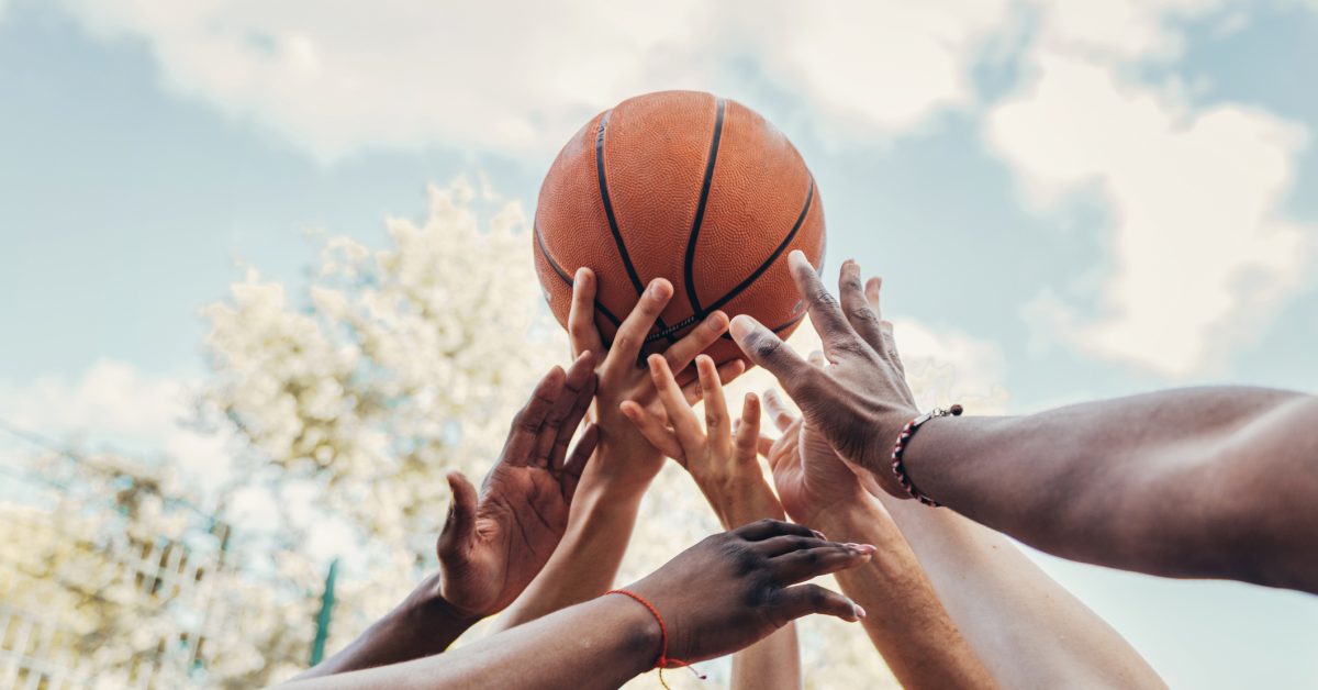 arms of multi ethic sports people are raised against sky multi-ethnic sports group raising arms holding basketball